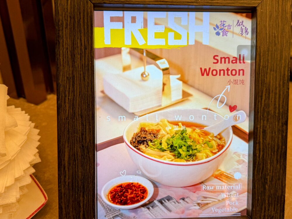 No.72ラウンジLIVEキッチンのメニュー写真。「Small Wonton(小馄饨)」の完成イメージ。スープワンタンにラー油が添えられた一品の写真が額縁に入って展示されている。