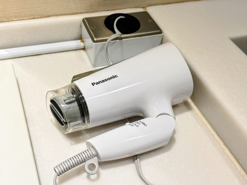 PanasonicのコンパクトドライヤーEH-KE0Aのクローズアップ。白いボディでTURBO・DRY・COLD・OFFの切り替えスイッチが側面に確認できる。洗面台の縁に置かれている。