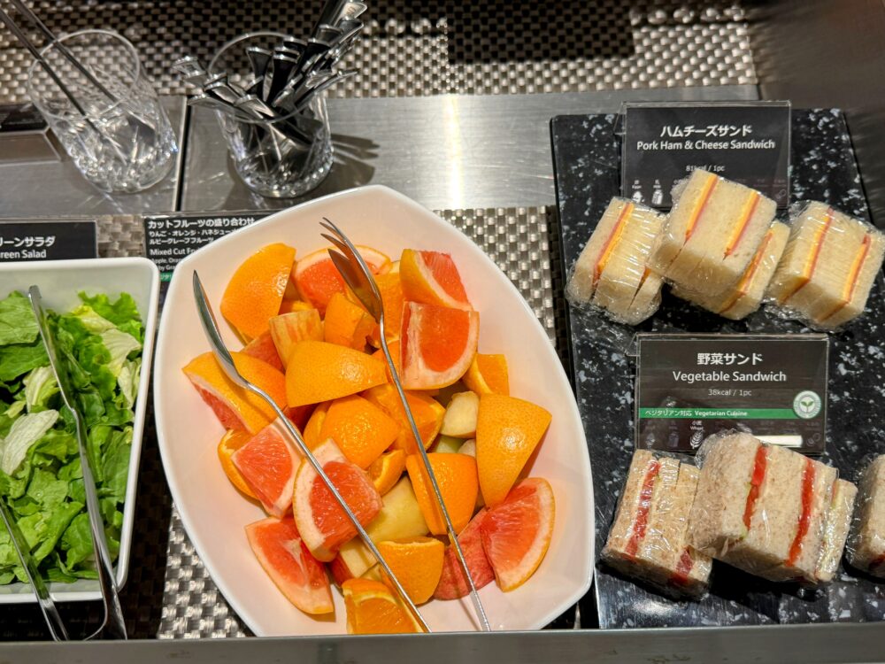 羽田空港第2ターミナル国際線ANAスイートラウンジのビュッフェコーナー。カットフルーツ（オレンジ・グレープフルーツ）とハムチーズサンド・野菜サンドが並ぶ。