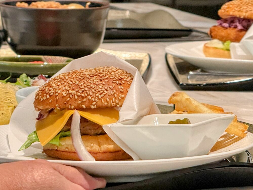 SUITE DININGで提供されるビーフチーズバーガー。チーズ・レタス・オニオンをたっぷり挟んだ本格バーガーにポテト添え。奥にはかつバーガーも見える。