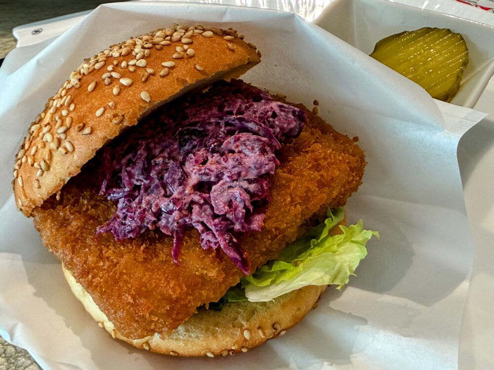 おからこんにゃくを使った"ヘルシー"かつバーガー。サクサクの衣に紫キャベツのコールスローをのせたバンズが白い皿に盛られ、ピクルス添え。