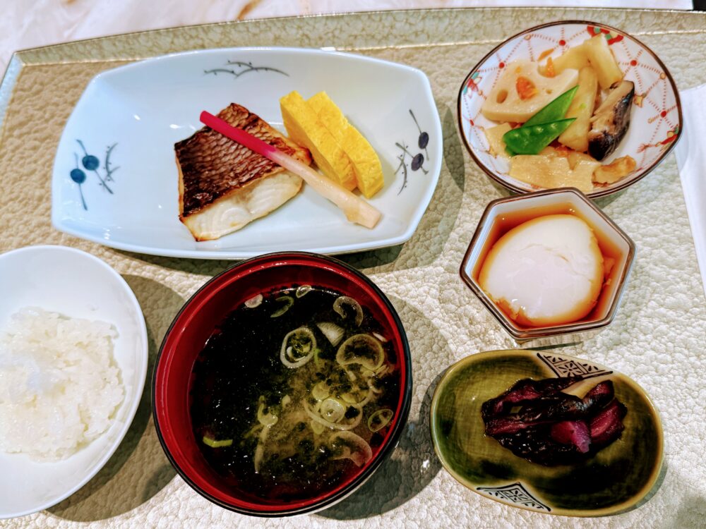 ANAスイートラウンジSUITE DININGの真鯛粕漬け焼き御膳。焼き魚・玉子焼き・煮物・温泉卵・お漬物・ご飯・わかめ味噌汁が金色のトレイに丁寧に盛り付けられた朝食。
