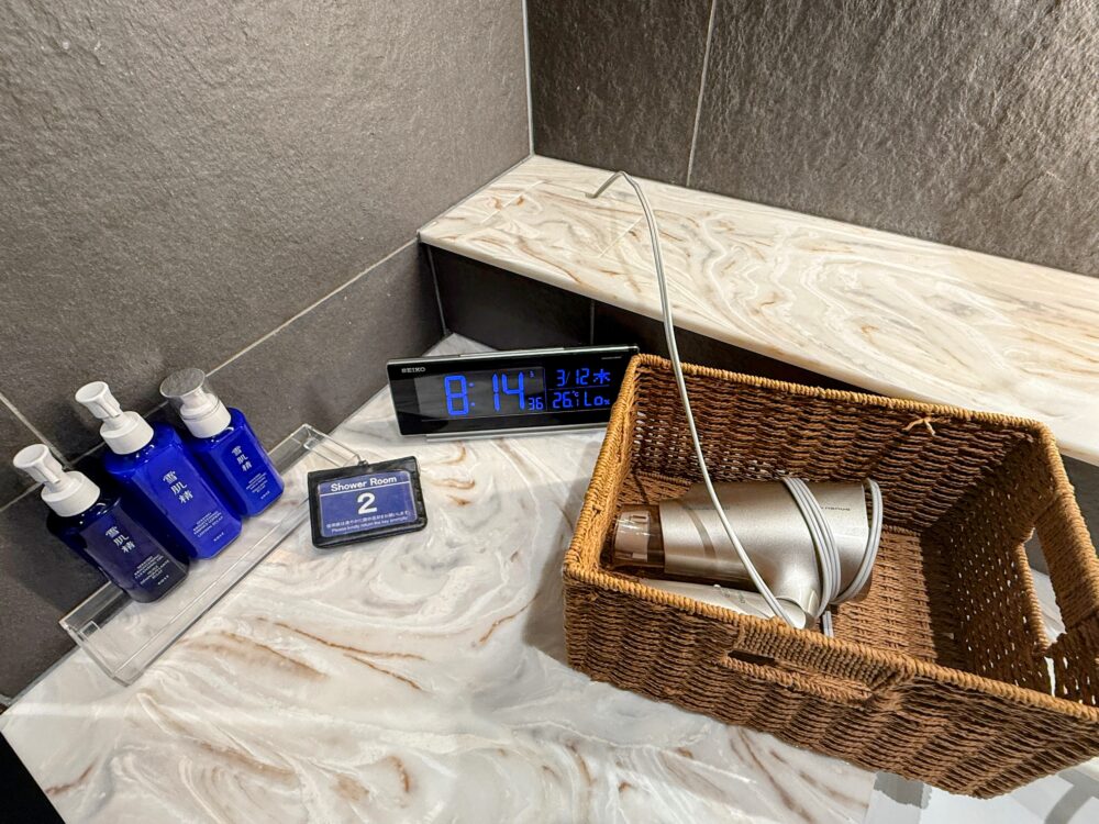 雪肌精スキンケアセット、SEIKOの時計、ドライヤーが用意されたシャワールームのカウンター。