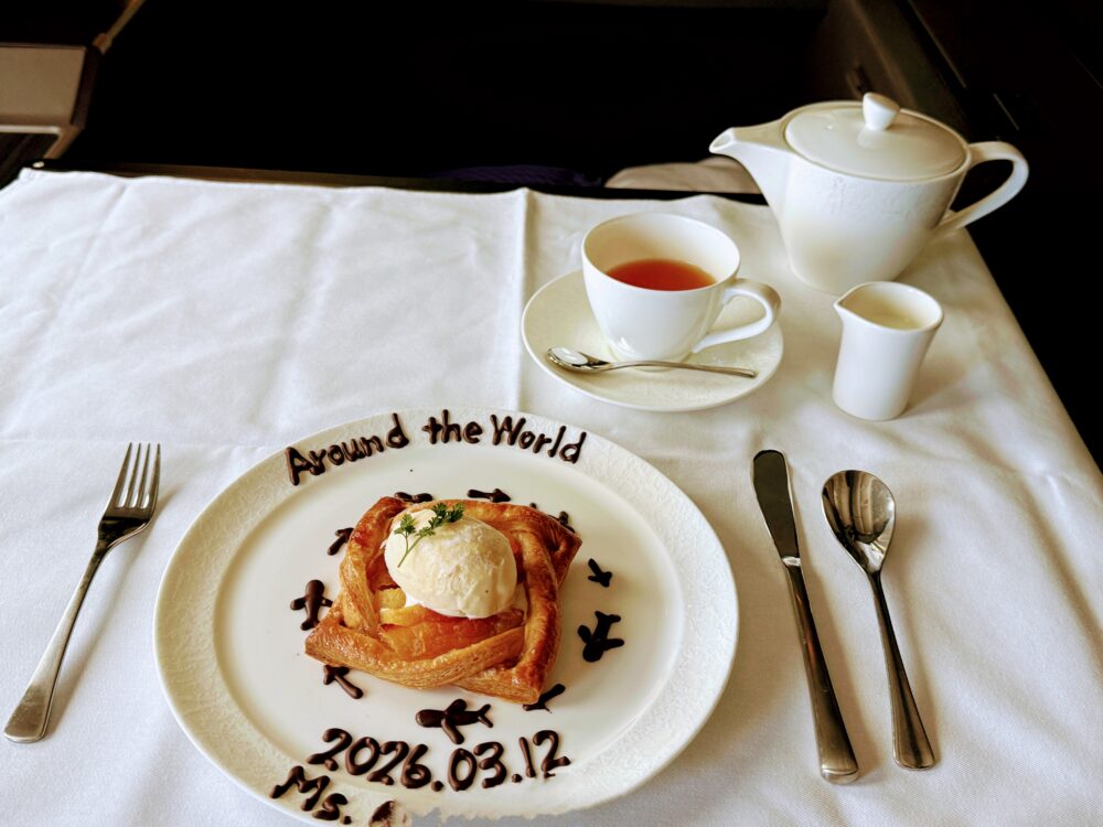 アップルパイとバニラアイスに「Around the World 2026.03.12 Ms.〇〇」のチョコレートメッセージ。紅茶のカップとティーポット添え。