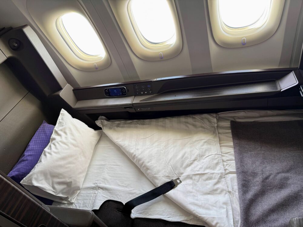 ANA THE Suite 1A席がフルフラットベッドに変わった状態。白いピローとデュベが整えられ、正面に3つの窓が並ぶ。窓の外には薄い雲が広がっている。
CAさんが整えてくださったベッド。窓3つを独り占めしながら眠れる、空の上の特等室です。