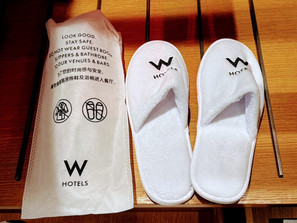 W上海のロゴが黒糸で刺繍された、ふかふかで厚みのある白い室内用スリッパと専用袋。
