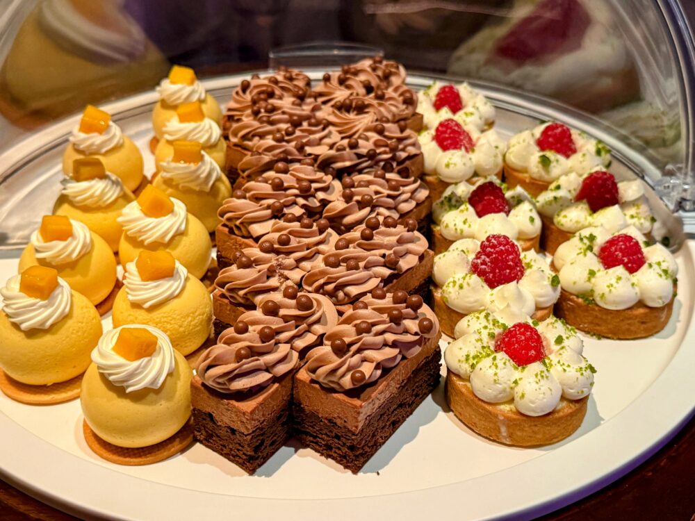 マンゴープリン、チョコレートブラウニー、ラズベリータルトなど、美しく並べられた一口サイズのスイーツ。