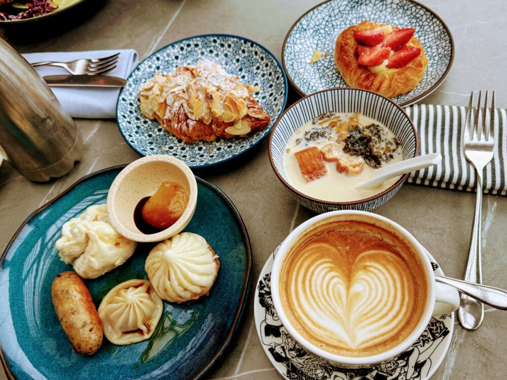 W上海の朝食ビュッフェで綺麗に盛り付けたテーブル。美しいラテアートのコーヒー、トッピングたっぷりのお粥、小籠包や肉まん、アーモンドクロワッサンやイチゴのデニッシュ。
