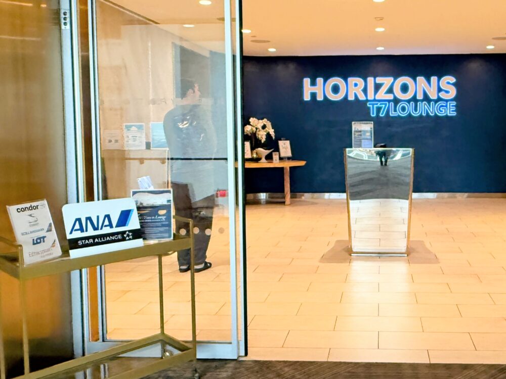 HORIZONS T7 LOUNGEの入口。ガラス張りの扉越しにレセプションデスクと「HORIZONS T7 LOUNGE」のネイビーのロゴウォールが見えます。