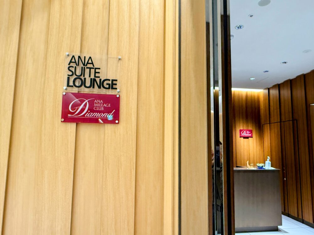 那覇空港ANAスイートラウンジの入口。「ANA SUITE LOUNGE」のロゴプレートと「ANAマイレージクラブ Diamond」の赤いサインが壁に掲げられ、奥にウェルカムカウンターが見える。