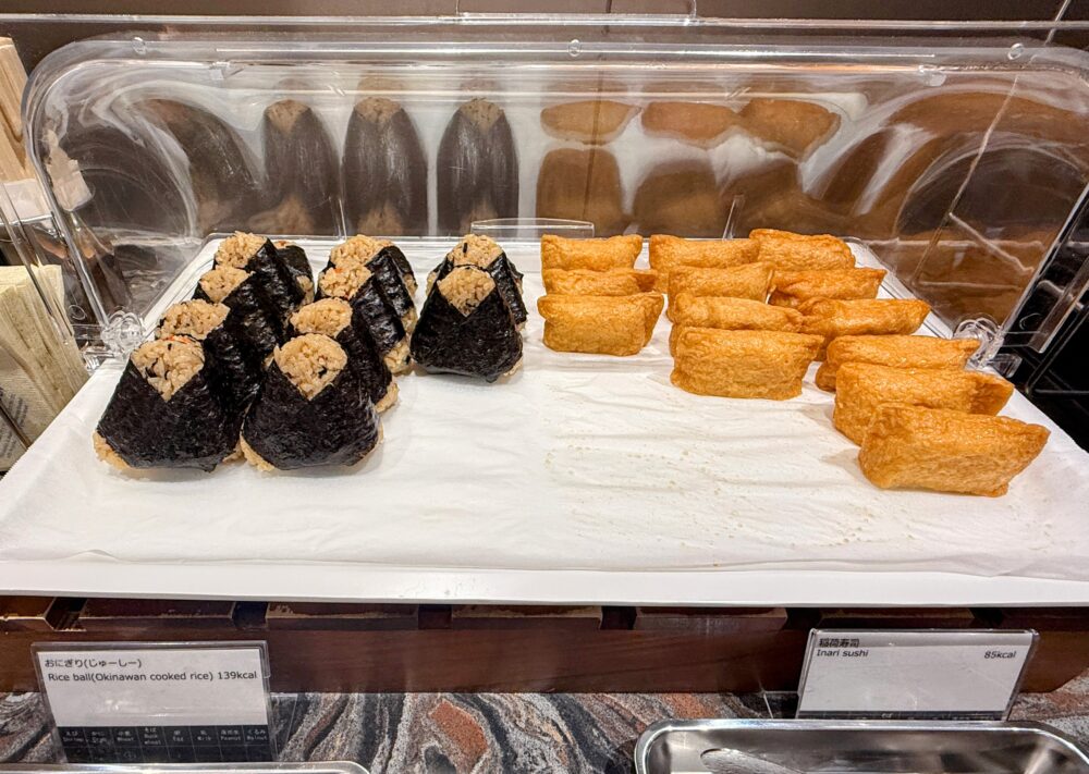 ラウンジの軽食コーナーに並ぶ沖縄風炊き込みご飯「ジューシー」のおにぎりと稲荷寿司。