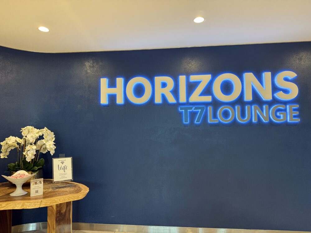 HORIZONS T7 LOUNGEのエントランスホール。ネイビーの壁に「HORIZONS T7 LOUNGE」の立体ロゴが輝き、手前の木製テーブルにWi-Fi案内カードと白い蘭の花が飾られています。