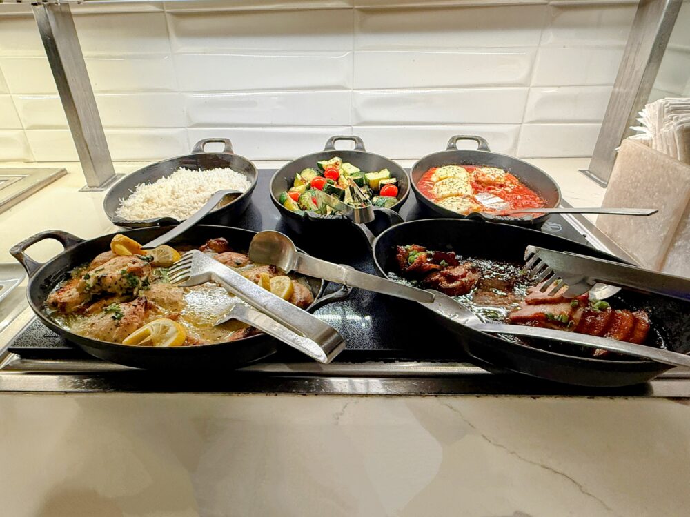 ファーストクラスラウンジのホットミールコーナー。レモンチキン、BBQポーク、トマトソースのフィッシュ、ライス、ズッキーニソテーが鉄製スキレットで温められています。
