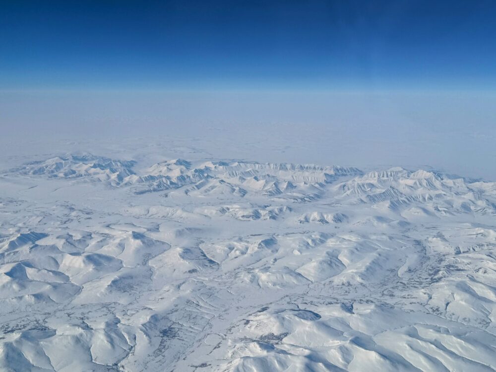 飛行機の窓から見下ろす、北極圏の果てしなく続く真っ白な雪山の絶景。