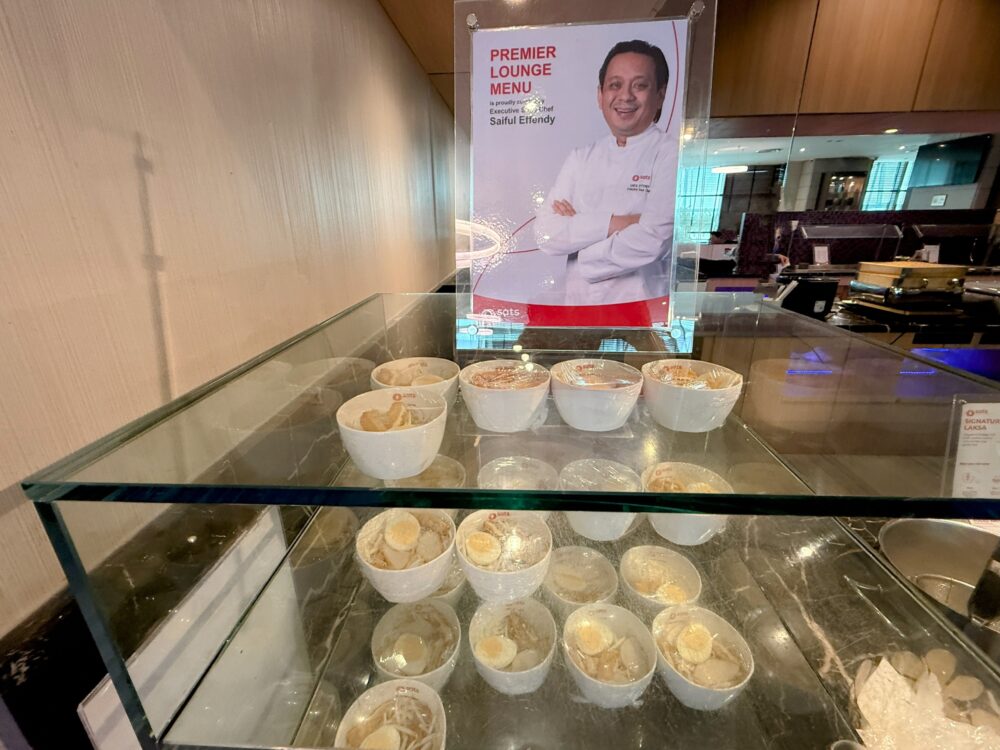 SATS Premier Loungeの看板メニューであるラクサのセルフサービスコーナー。調理方法が掲示され、麺の入ったお椀が並んでいる。