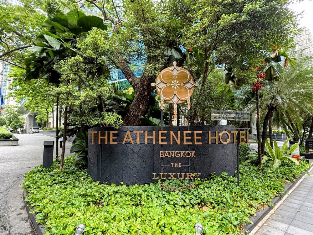 緑に囲まれた「THE ATHENEE HOTEL BANGKOK」のエントランスサイン。マリオット系列ラグジュアリーコレクションのロゴが掲げられたアテネホテル バンコクの入口。