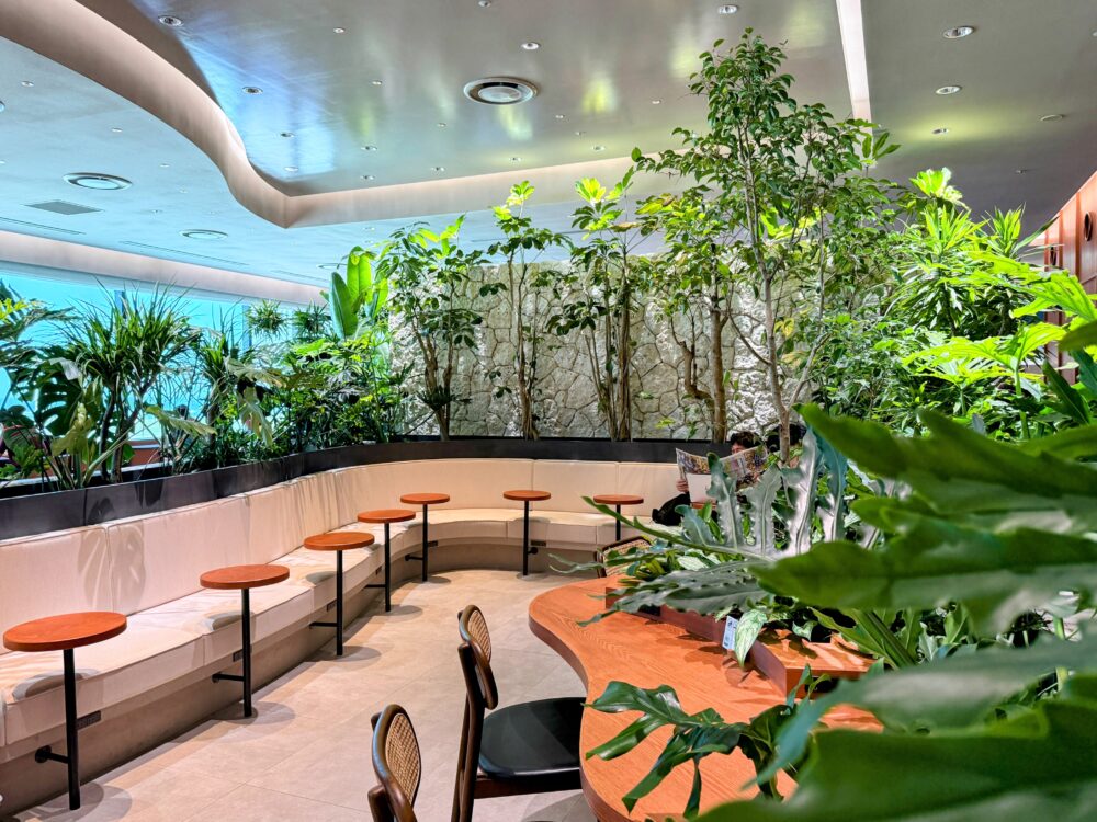 那覇空港カードラウンジ「LOUNGE HANA」のボタニカルガーデン風エリアに並ぶ白いソファ席と丸テーブル