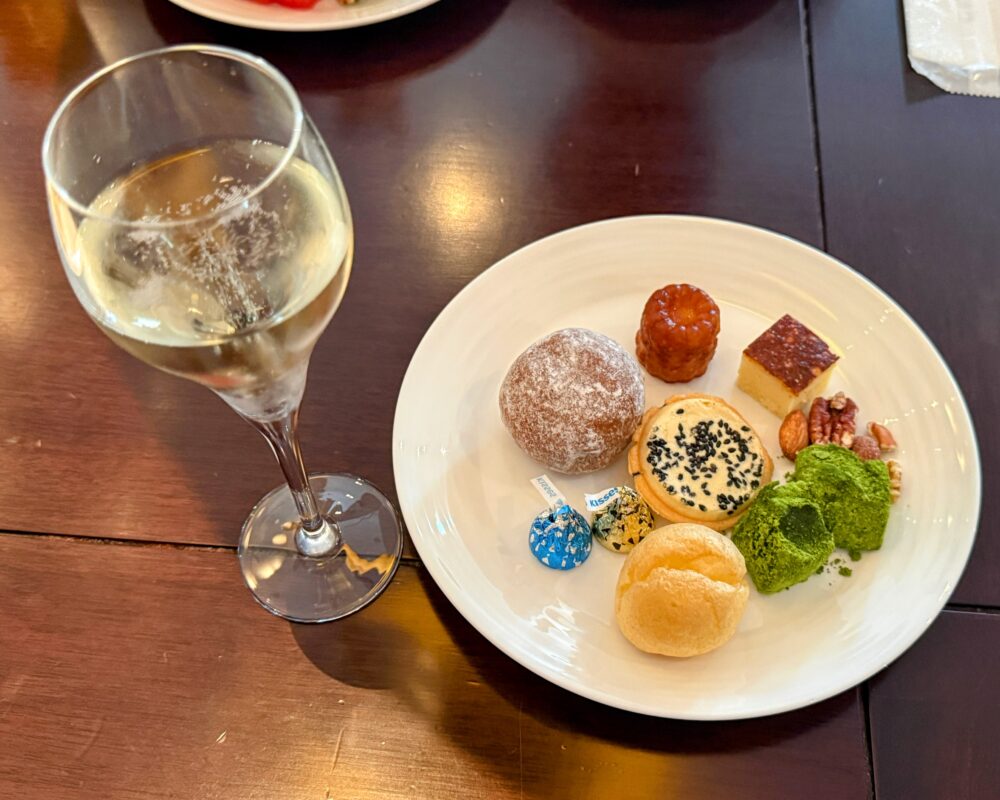 アフタヌーンティーのデザートを盛り付けた皿とシャンパングラス。わらびもち・カヌレ・抹茶の生チョコなど