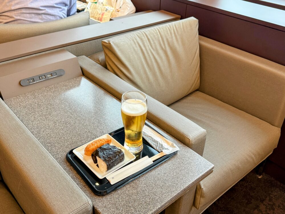 滑走路に面した窓際のソファ席。ビールといなり寿司・おにぎりをのせたトレーを置き、飛行機を眺めながらくつろげる特等席。