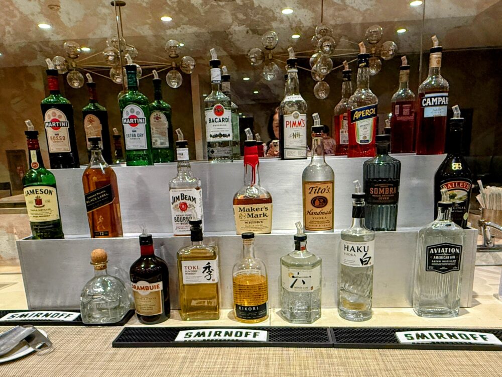 ファーストクラスラウンジのバーカウンターに並ぶスピリッツのボトル。Jameson、Jim Beam、Maker's Mark、Toki、Tito's Vodka、HAKU Vodka、Bailey's、Aviation Ginなど多彩なラインナップが揃っています。