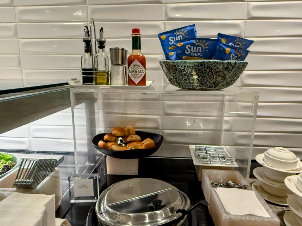ビジネスクラスラウンジのフードステーション。タバスコやオリーブオイルの調味料、Carrot Ginger Soupのスープ鍋、ロールパン、Sun Chipsが並んでいます。