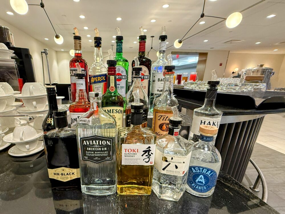 ビジネスクラスラウンジのスピリッツコーナー。Aviation Gin、Toki Whisky、HAKU Vodka、Astral Tequila、Aperol、Martini、Campari、Jamesonなど多彩なボトルが並んでいます。