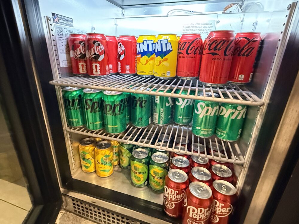 ビジネスクラスラウンジの冷蔵庫内のソフトドリンク。Coca-Cola、Fanta、Sprite、Seagram's、Dr Pepperなどの缶が3段に並んでいます。
