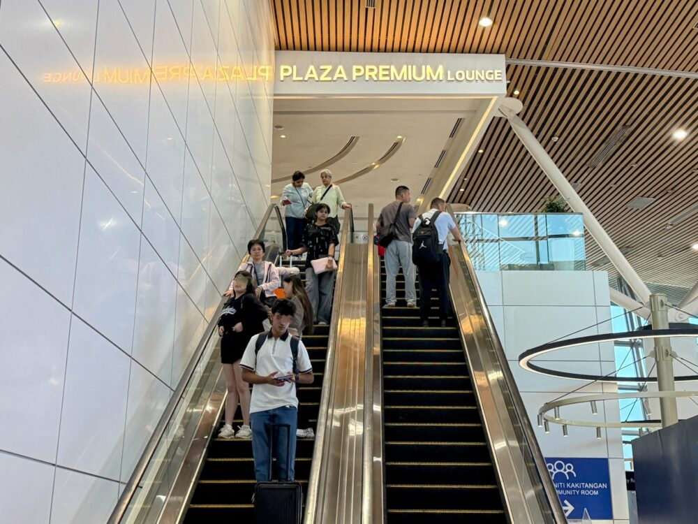 プラザプレミアムラウンジへと続くエスカレーターに乗る多くの旅行客と上部の看板