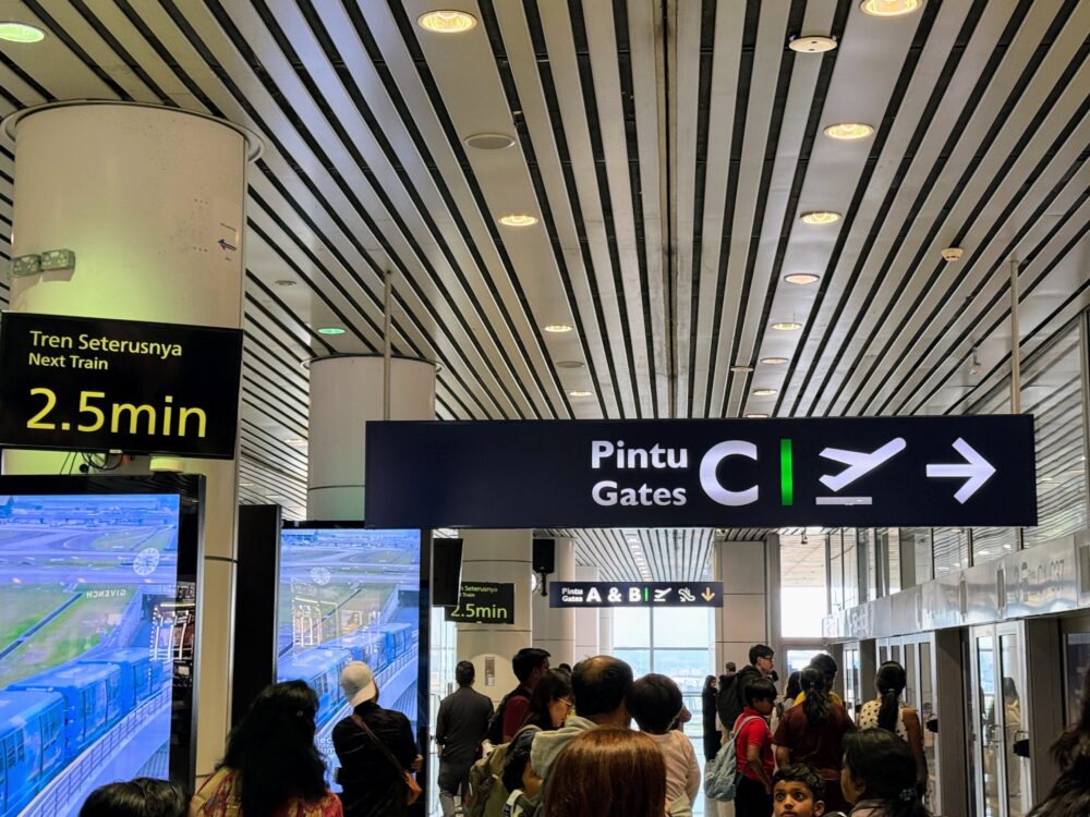 クアラルンプール国際空港(KLIA)第1ターミナルで、サテライトへ向かうエアロトレイン乗り場に並ぶ旅客と案内サイン