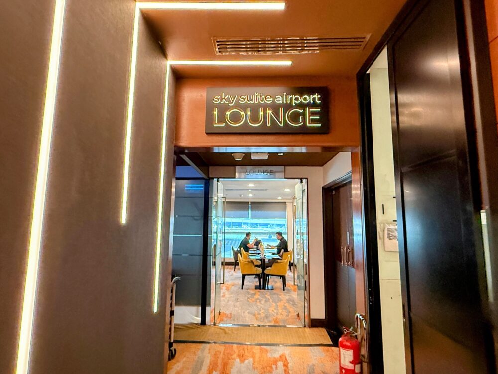 暖色系の間接照明とゴールドの立体文字で「sky suite airport lounge」と掲げられたラウンジの入口通路