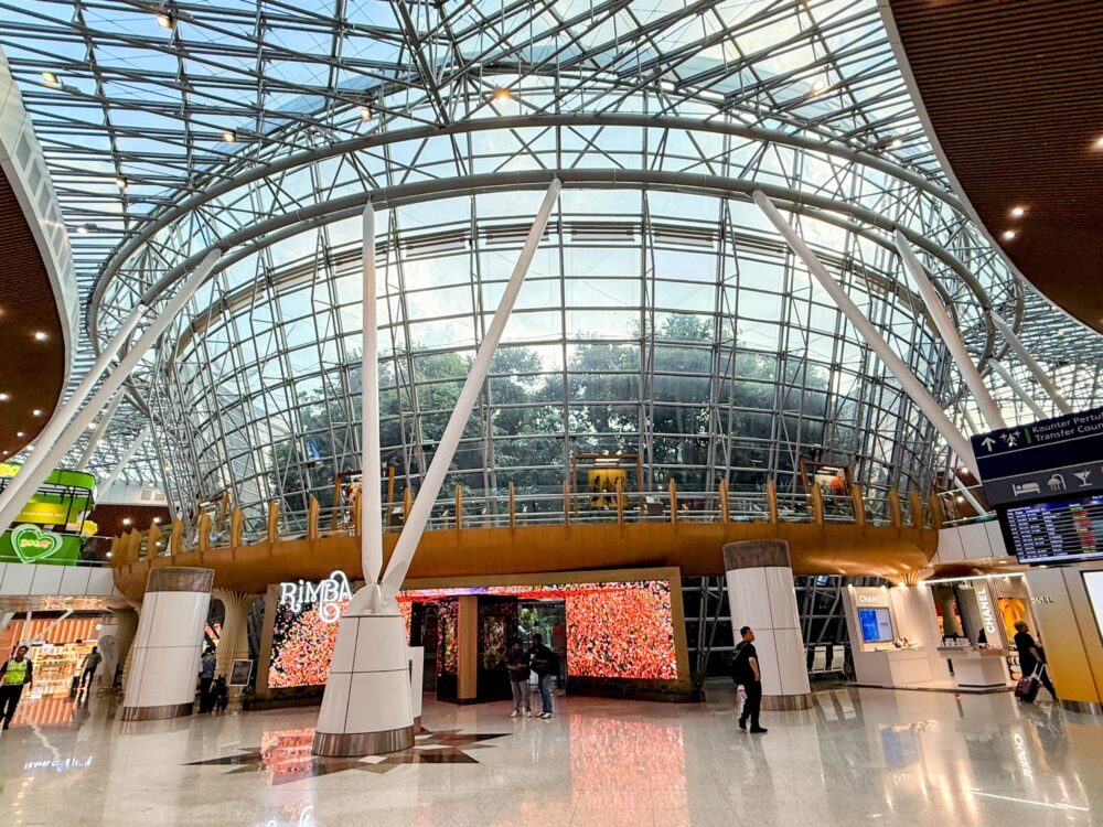 クアラルンプール空港サテライトビル中央の屋内庭園「RIMBA」。巨大なガラスドームの下に熱帯の木々と木製の空中回廊が広がっている