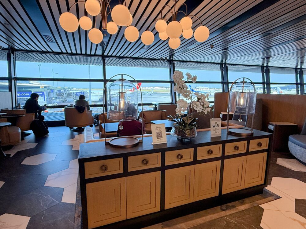 「GLOBAL LOUNGE」の滑走路側シーティングエリア。大きな窓の外に駐機中の航空機が見え、手前のカウンターには白いランの花やドーム型のテーブルランプが飾られている。
