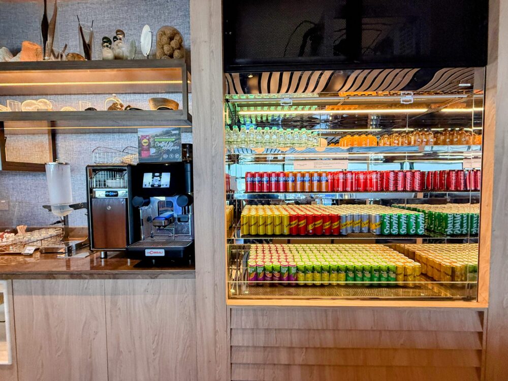 「GLOBAL LOUNGE」のドリンクステーション。黒いコーヒーマシンの隣に、色鮮やかな缶ジュースやペットボトルがぎっしりと並んだ冷蔵ショーケースが設置されている。