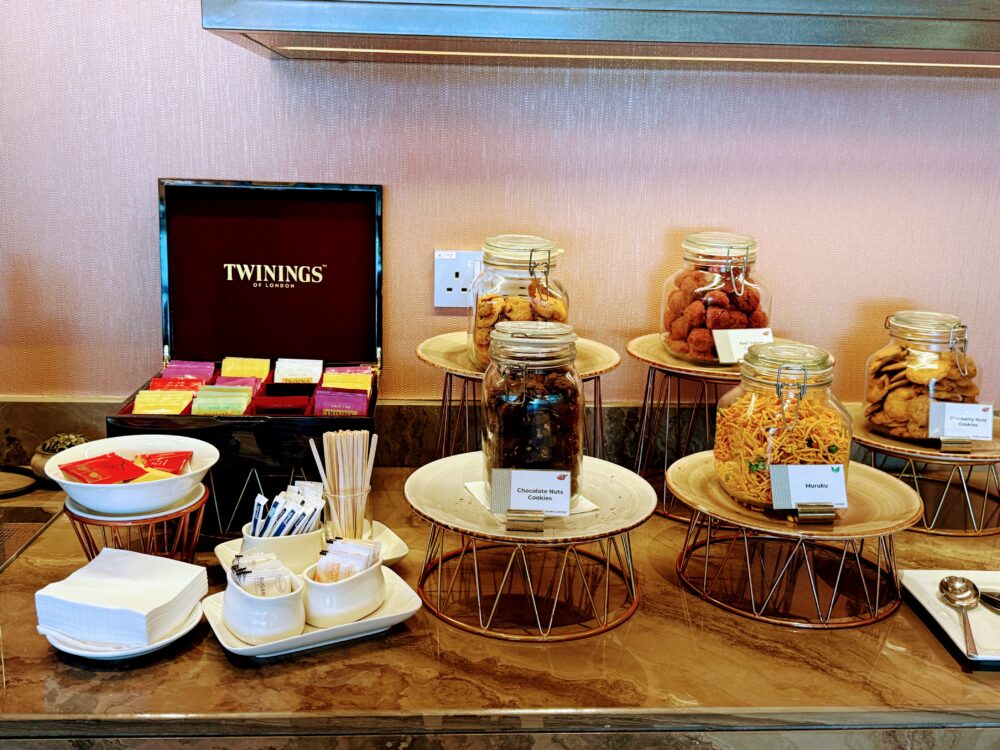 「GLOBAL LOUNGE」のクッキーとティーバッグのコーナー。TWININGSの紅茶が収納された木製ボックスの横に、チョコレートナッツクッキーやクランベリーナッツクッキー、スナック類を入れたガラス瓶が並んでいる。