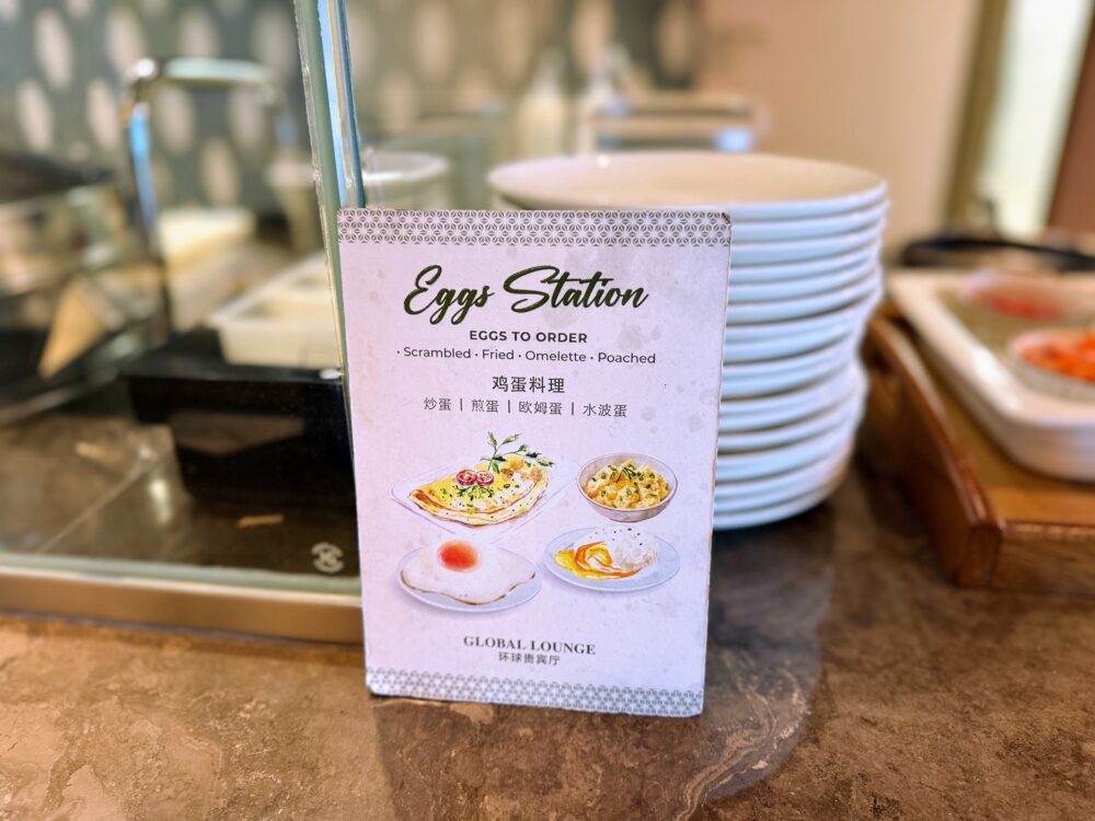 「GLOBAL LOUNGE」のエッグステーションの案内板。注文できる卵料理（スクランブル、目玉焼き、オムレツ、ポーチドエッグ）が英語と中国語で記載され、それぞれの料理のイラストが添えられている。