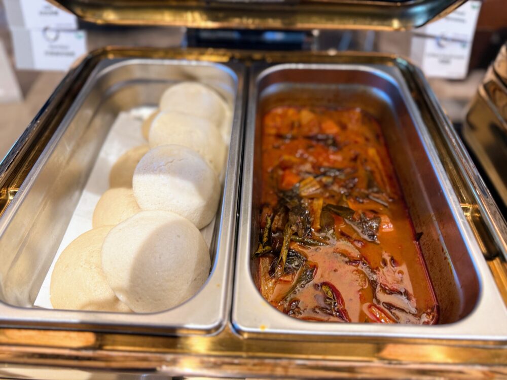 温かいスチーム料理と煮込み料理のホットビュッフェ。左側にはふっくらとした白い蒸しパン（パオ）、右側にはスパイシーなスープや煮込み料理が入っている。