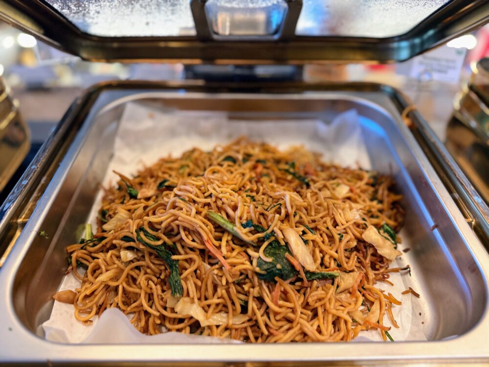 「GLOBAL LOUNGE」のホットビュッフェにある焼きそば（ミーゴレン風の麺料理）。野菜や細切れの具材と一緒に香ばしく炒められたヌードルが、バットに敷かれたクッキングシートの上に盛られている。