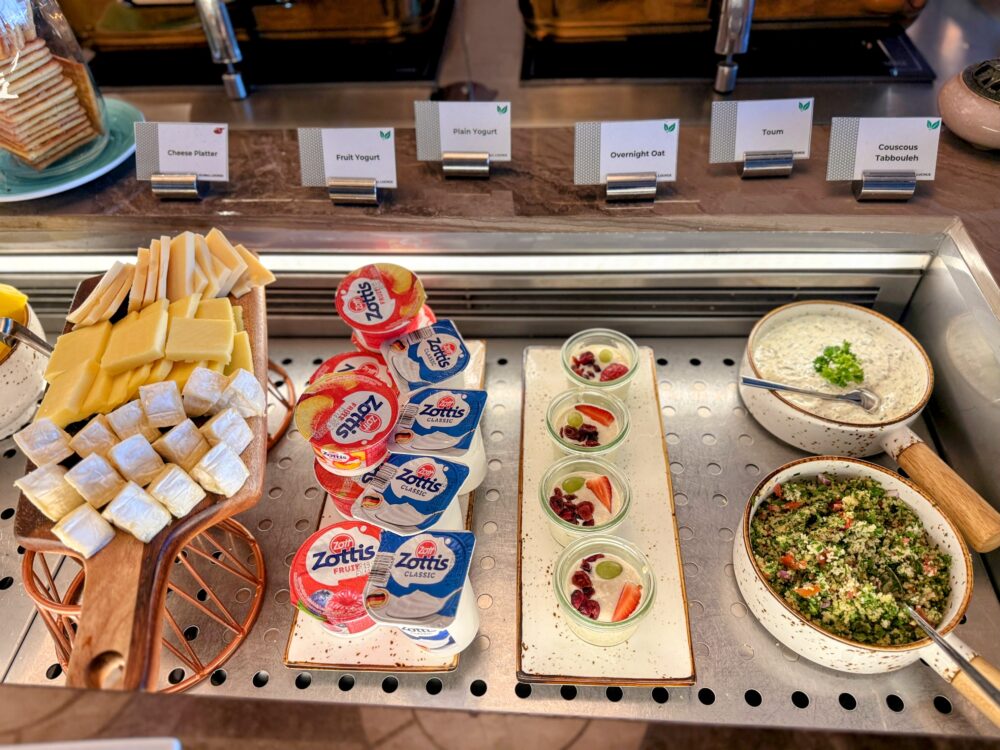 「GLOBAL LOUNGE」のチーズ・ヨーグルト・冷製サラダコーナー。カットされた各種チーズや、カップヨーグルト、グラスに入ったフルーツ入りオーバーナイトオーツ、ディップソースやタブーリサラダが並んでいる。