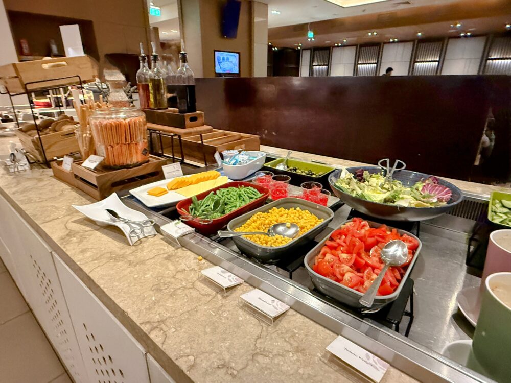 プラザプレミアムラウンジのサラダバー。トマト、コーン、インゲン、オリーブ、各種ドレッシングボトルやクラッカーなどが並ぶビュッフェの様子。
