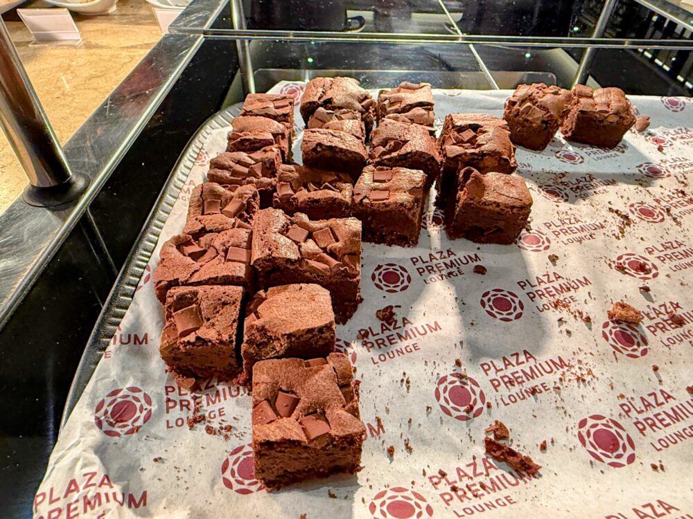 プラザプレミアムラウンジのデザートコーナー。「PLAZA PREMIUM LOUNGE」のロゴが敷かれたペーパーの上に並ぶチョコレートブラウニー。