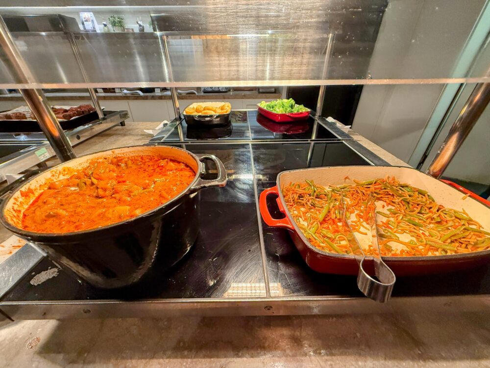 プラザプレミアムラウンジのホットミールカウンター。煮込み料理が入った黒い大鍋と、野菜の炒め物が入れられた赤いサービング皿。
