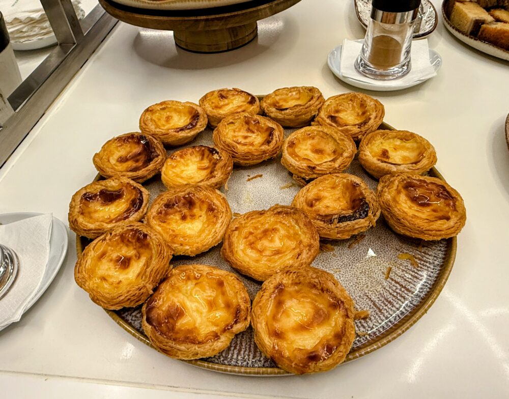 エッグタルトが美しく盛り付けられた丸い皿のクローズアップ。こんがりと焼き色がついたパイ生地とカスタードの焼き目が食欲をそそる仕上がりで、周囲には調味料入れや取り皿が配置されている。