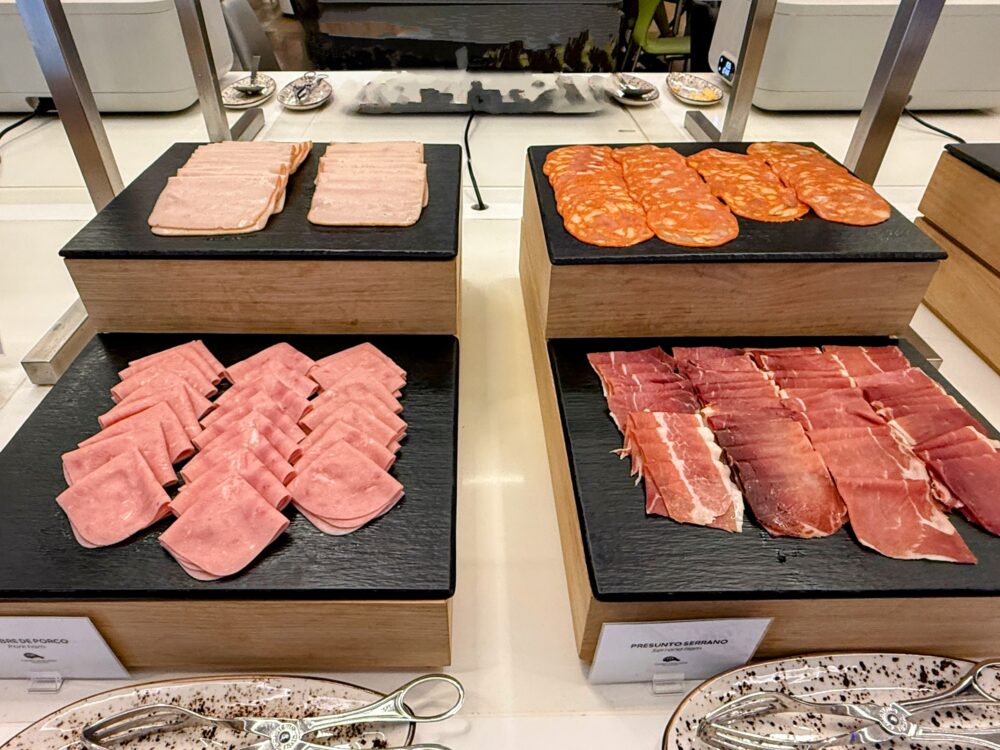 黒い石目調の台に陳列された冷製シャルキュトリー(肉加工品)のコーナー。上段にはスライスされたハムやサラミ、下段には美しいサシの入った生ハム(Presunto Serrano)やポークハムが綺麗に並べられている。