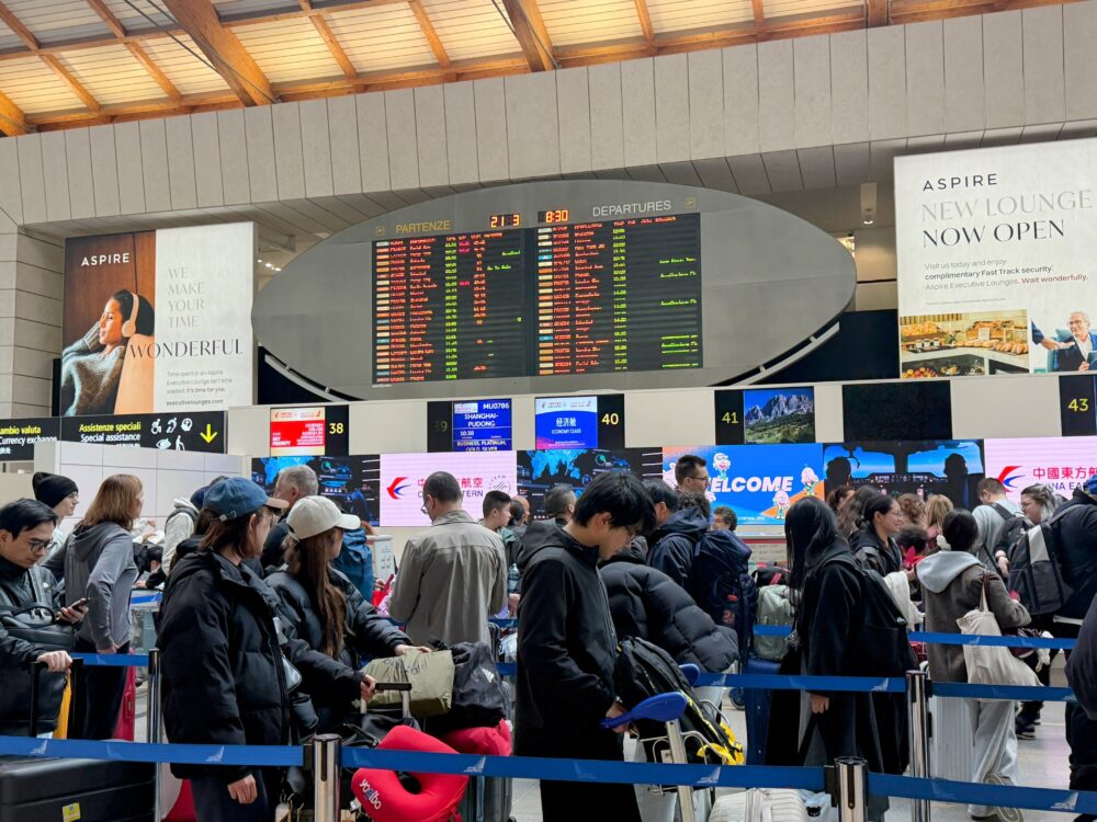 「ASPIRE NEW LOUNGE NOW OPEN/complimentary Fast Track security」と大きく掲出されたAspire Executive Loungeの広告と、楕円形の枠に収まったベネチア空港の出発案内板。