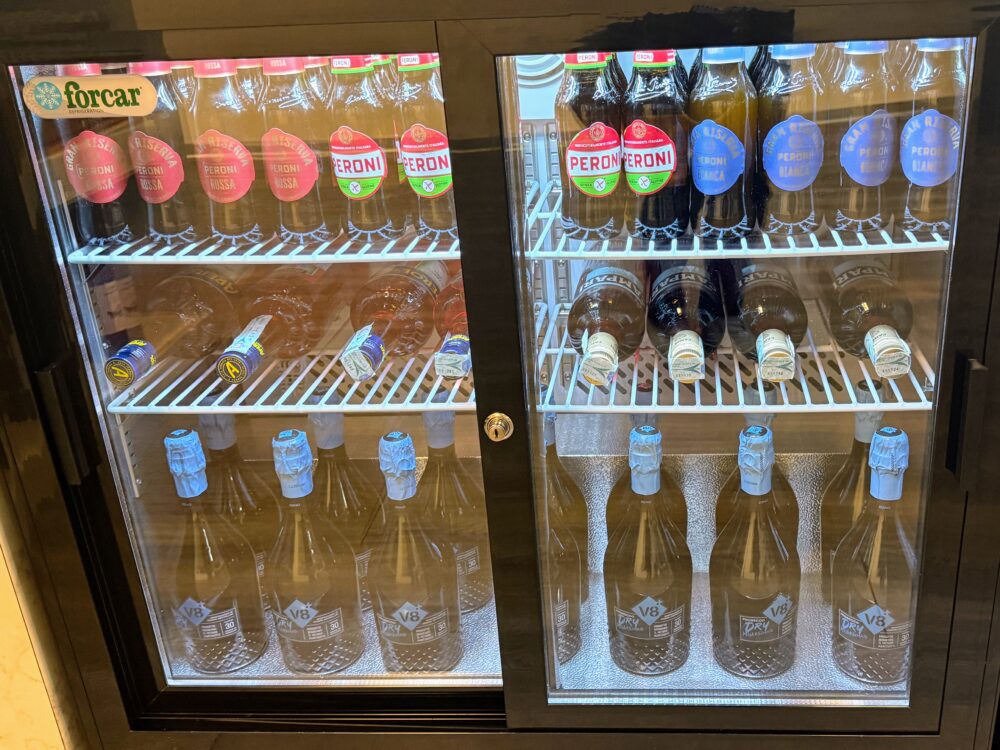 「forcar」のロゴがあるガラス張りの冷蔵庫に並ぶ、ペローニ(Peroni)のビールボトルやプロセッコ(V8+)のボトル。