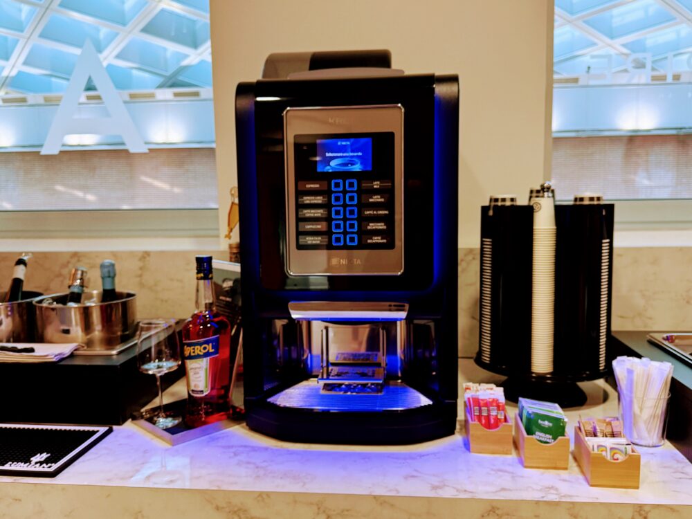 青い照明でライトアップされた全自動コーヒーマシンと、その隣に設置されたアペロール(Aperol)のボトルやカップ・ティーバッグのセット。