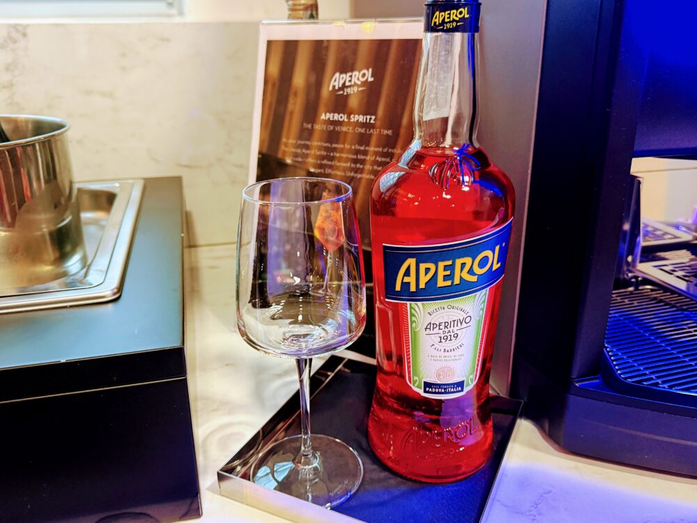 「APEROL SPRITZ」の案内板の横に置かれたアペロールのフルボトルと、グラスが用意されたドリンクコーナーの一角。