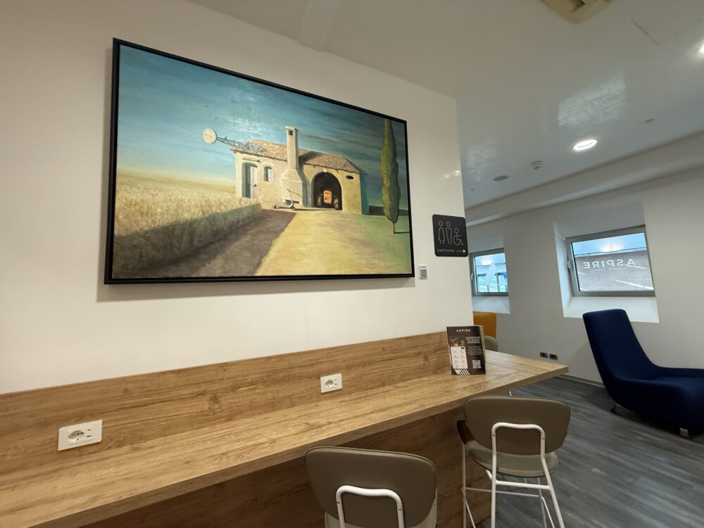 田園風景を描いた大きな絵画が飾られた木製のハイカウンター席と、奥に見える青いリラックスチェア。