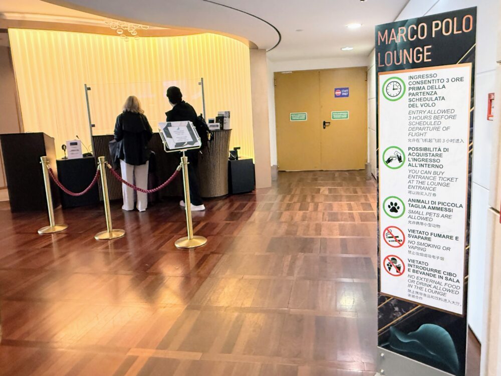 受付カウンターで手続きをする利用客と、入室条件(出発3時間前まで、ペット同伴可、禁煙など)が記載された縦型の案内看板。