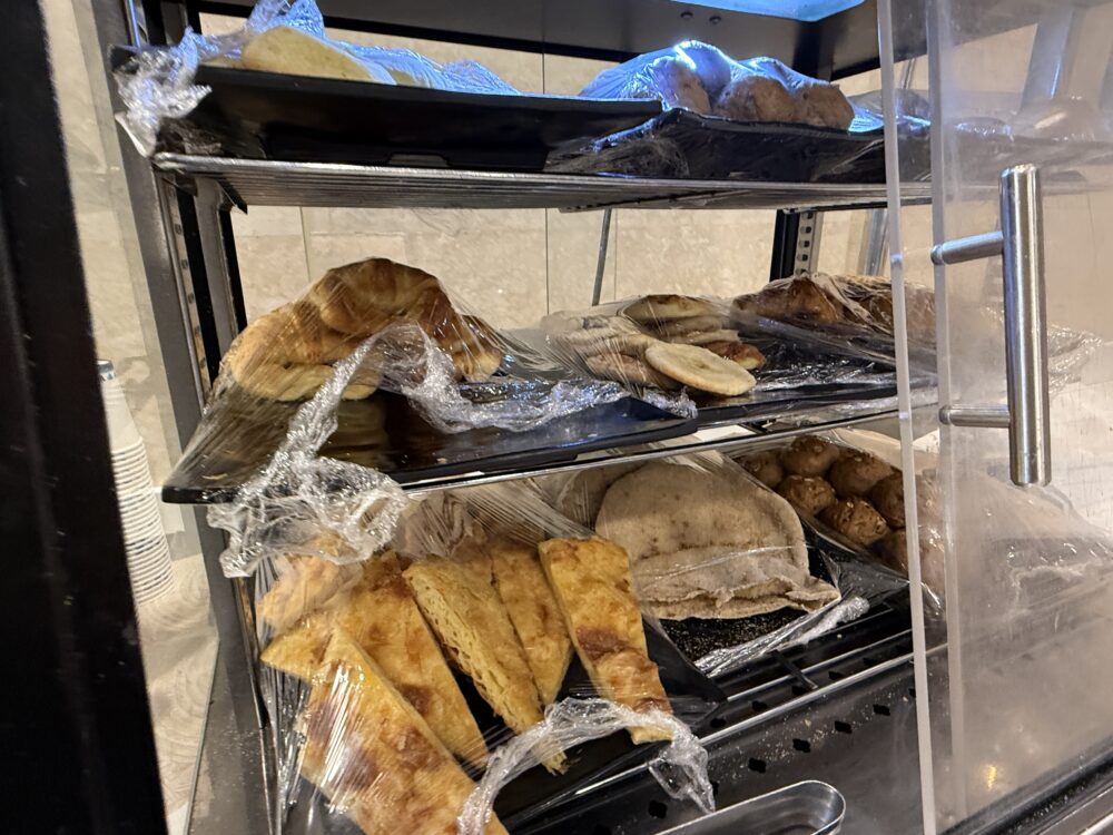 ガラスケースの中にラップで丁寧に包まれて並ぶ、数種類のパンやピタパン、ペイストリー類。